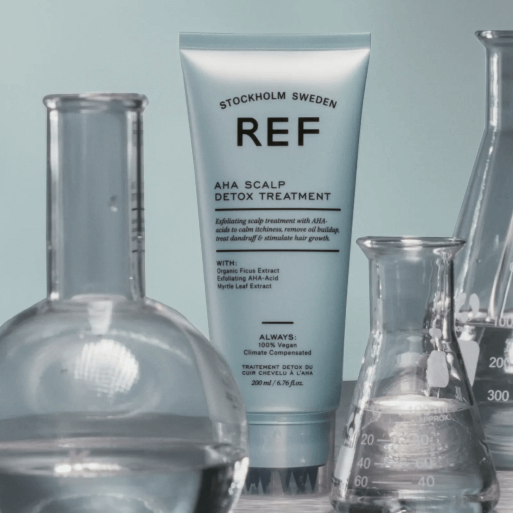 Tube of Stockholm Sweden REF AHA Scalp Detox Treatment surrounded by glass beakers on a light blue background