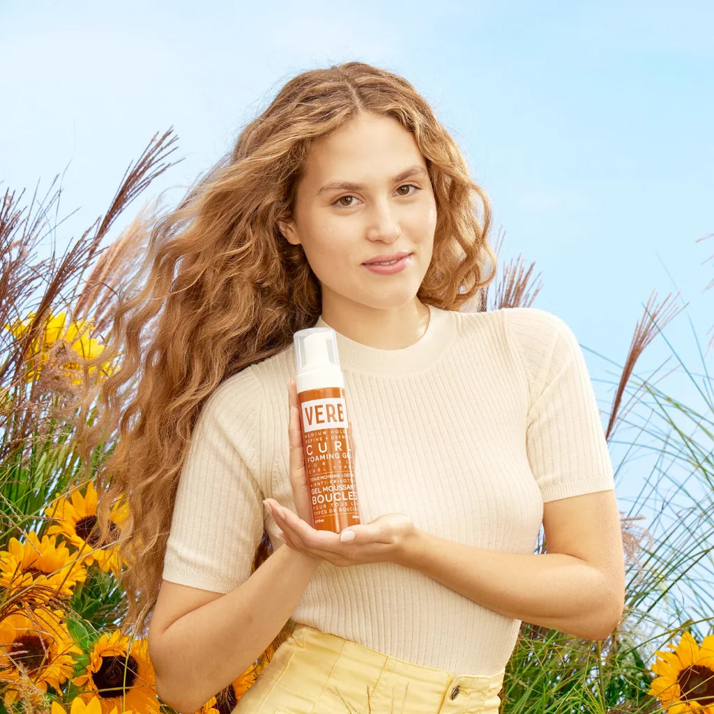 Woman holding a bottle of 'Vere' product in a sunflower field