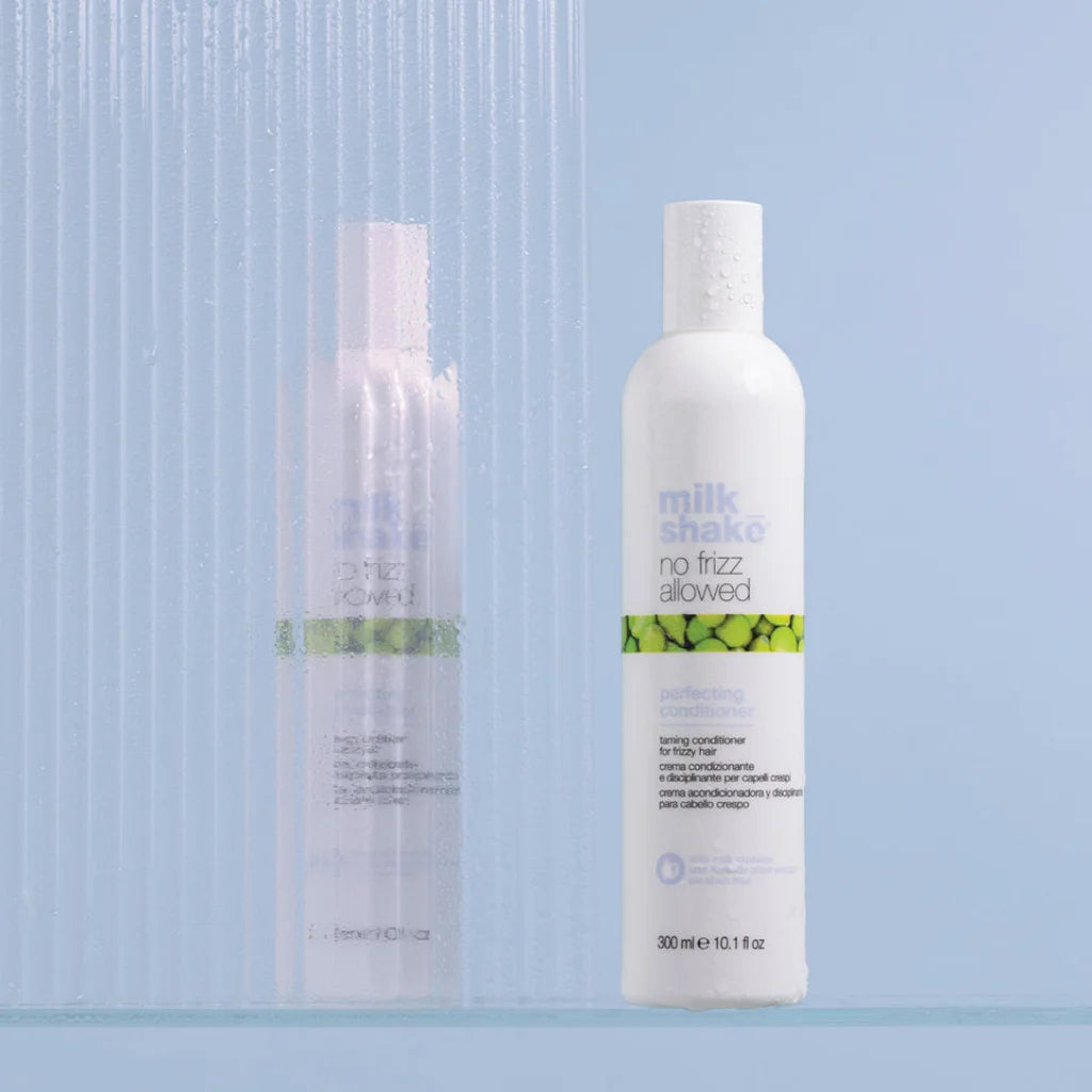Two Milk Shake haircare bottles on a light blue background, with a white bottle in front labeled 'milk shake no frizz allowed perfecting conditioner' and a translucent pale bottle behind it.