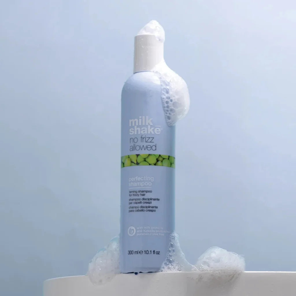 Bottle of 'milk shake no frizz allowed' shampoo with bubbles on a light blue background